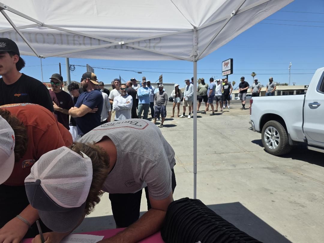 A crowd of anglers lined up under a white canopy tent