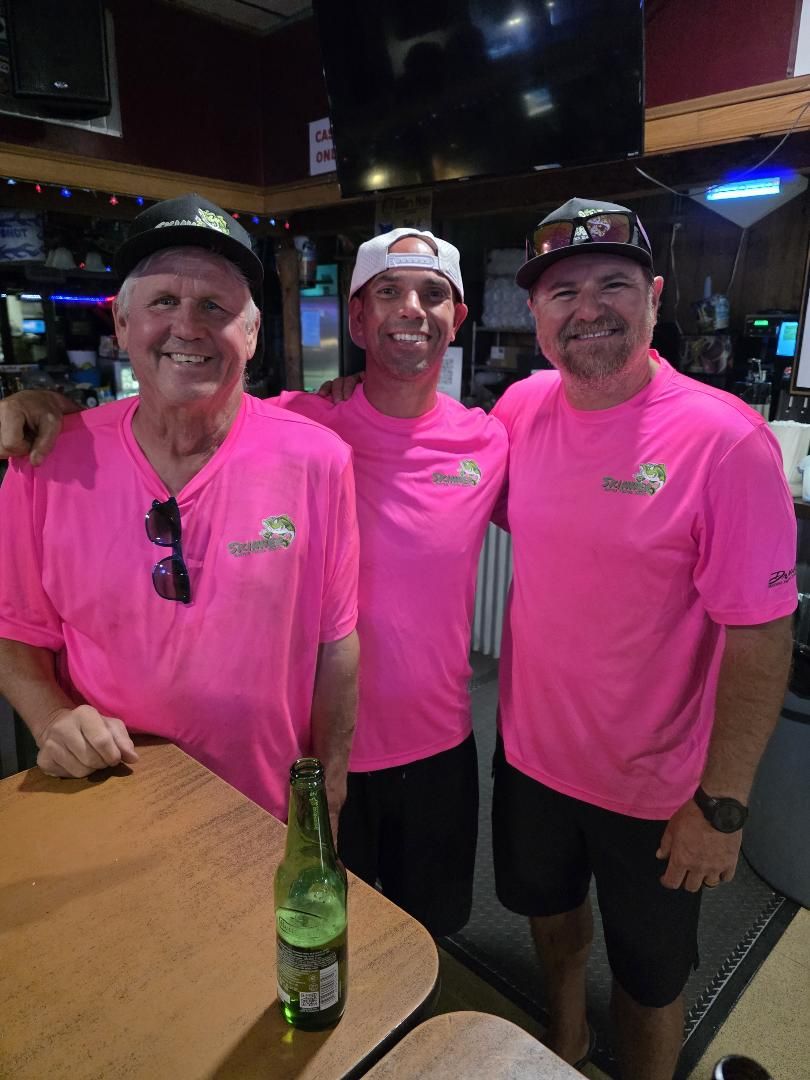 Three members of the crew in pink Skinner shirts smiling at a bar
