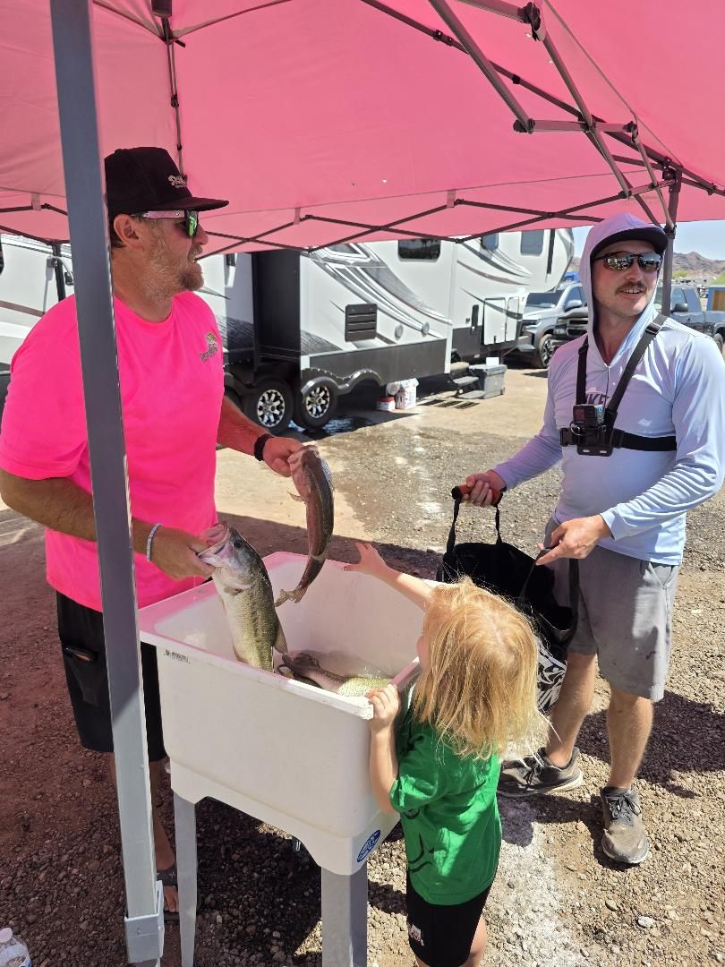 Billy in a pink shirt at the weigh tub while a child reaches toward the fish