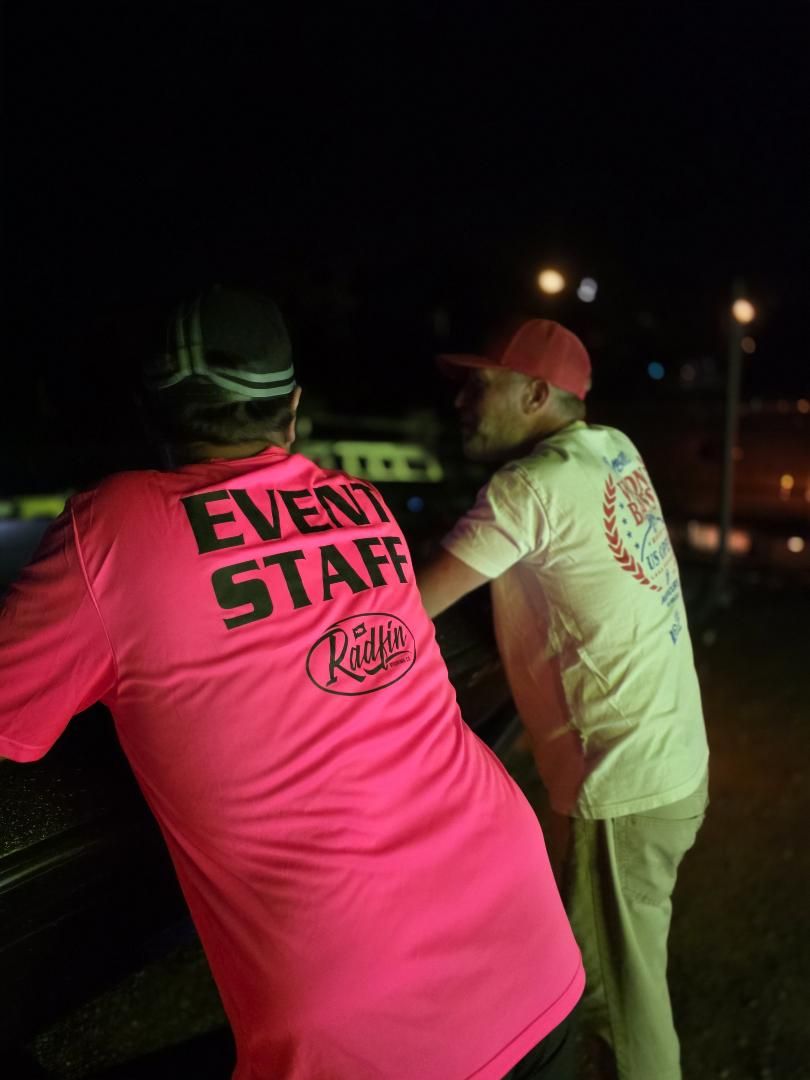 An event staff member in a pink shirt leaning on a truck at night