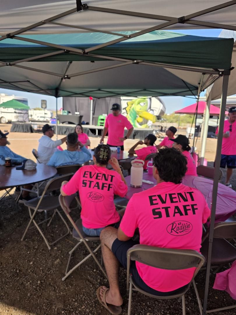 Event staff in pink shirts seated under a canopy before the event